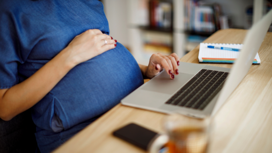 Schwangere Frau sitze am Schreibtisch mit Laptop